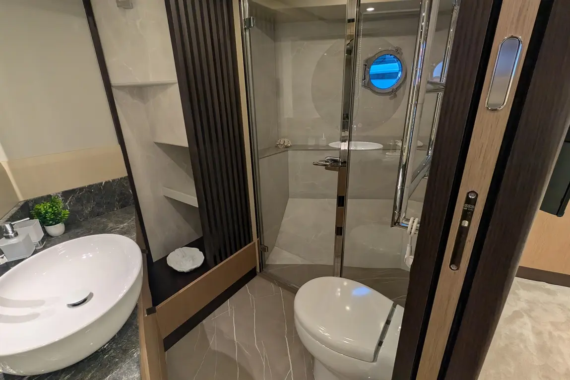 Modern bathroom with a glass shower, oval sink, toilet, and decorative plant on a marble countertop.